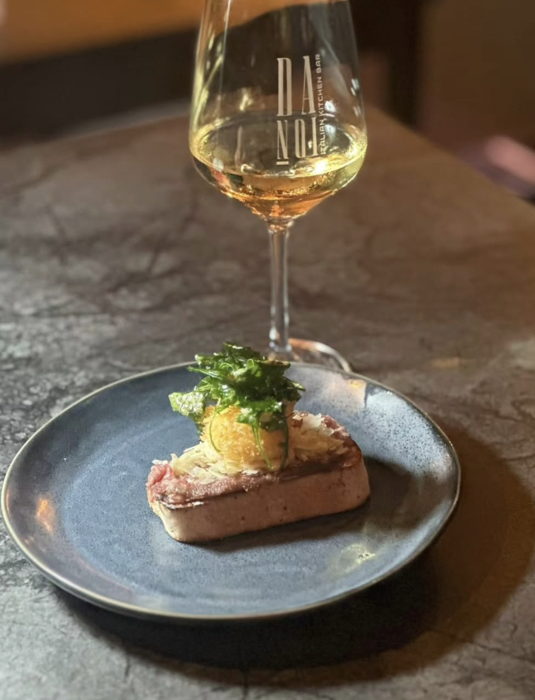 Glas Weißwein und liebevoll angerichtetes Gericht bei warmem Licht